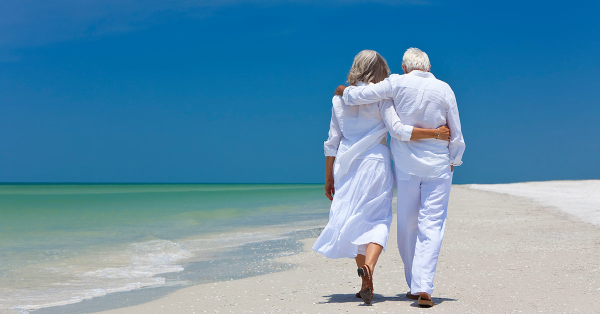 Ein älteres Paar läuft Arm in Arm am Strand entlang - Immobilienverrentung
